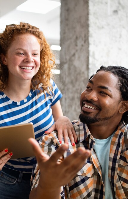 A white woman looking at a laptop having a conversation with a black man sitting on a chair in front of her