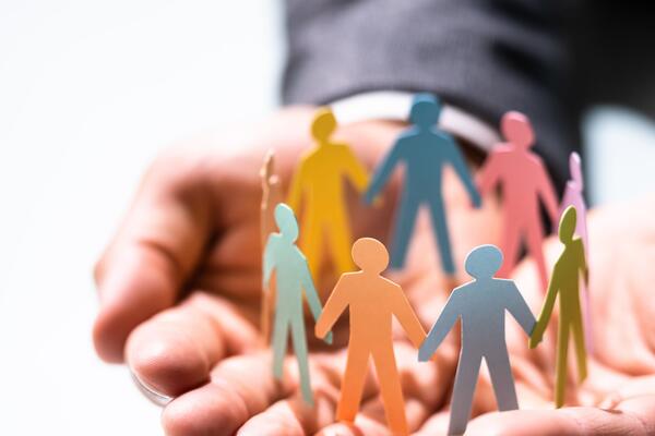 A group of colourful people figures made out of paper holding hands in a circle placed on a man's hands