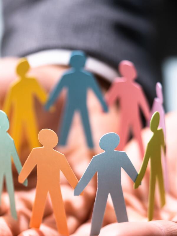 A group of colourful people figures made out of paper holding hands in a circle placed on a man's hands