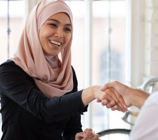 Une femme asiatique souriante portant un hijab rose serre la main d’une autre personne