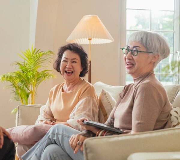Deux femmes asiatiques d'un certain âge assises sur un divan en train de rire. 