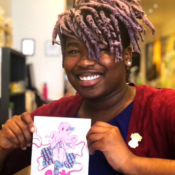 Une femme noire joyeuse tenant un papier avec l'illustration d'une pieuvre. 