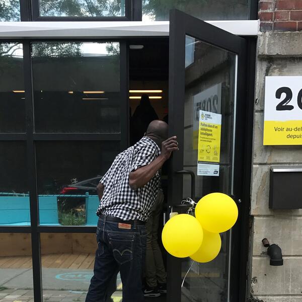 Un homme entre dans le Hub d'INCA. La porte est décorée de ballons jaunes